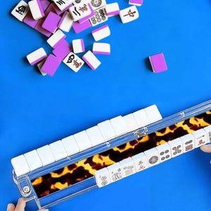 May include: A complete Mahjong set with white tiles and purple accents, scattered on a bright blue surface. The tiles are arranged in a clear case with a tortoiseshell pattern. The game set includes a variety of symbols and characters.