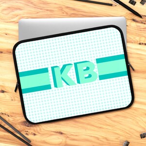 May include: A teal blue laptop sleeve with a white background and a teal blue polka dot pattern. The sleeve has a teal blue stripe with the letters "KB" in a 3D teal blue font.