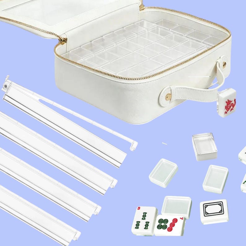 May include: White faux leather mahjong set with a gold zipper and handle. The interior has a clear plastic tray with multiple compartments. Includes white tiles, racks, and a decorative red and gold accent.