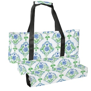 May include: A white tote bag with a blue and green floral pattern. The bag has black handles and a matching pattern on the folded bottom. The floral design features blue roses and green leaves.