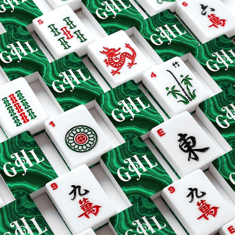 May include: A close-up shot of a Mahjong set with white tiles featuring red and green symbols and characters. The tiles are arranged in rows, with each tile resting on a green and white patterned surface. The set includes tiles with numbers, bamboo, and Chinese characters.