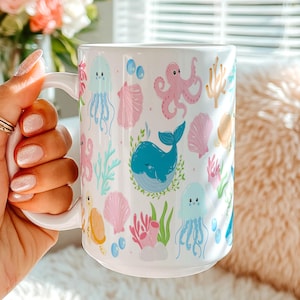 May include: A white ceramic mug featuring a repeating pattern of colorful sea creatures and ocean elements, including a blue whale, pink octopus, light blue jellyfish, orange sea turtle, various seashells, and green coral sprigs.