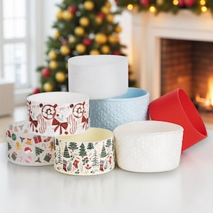 Puede incluir: Un conjunto de cuencos decorativos de cerámica con diseños navideños festivos. Los cuencos presentan varios patrones, incluyendo copos de nieve, árboles y adornos, en colores como el rojo, blanco y verde. También se incluye una funda de silicona roja.