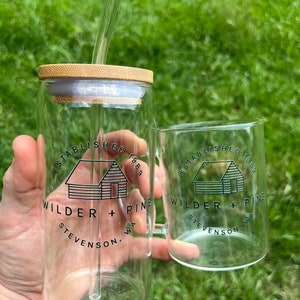 May include: Two clear glass mugs with a bamboo lid and a straw. The mugs have a black and white logo that says "Established 1889 Wilder + Pine Stevenson, WA".