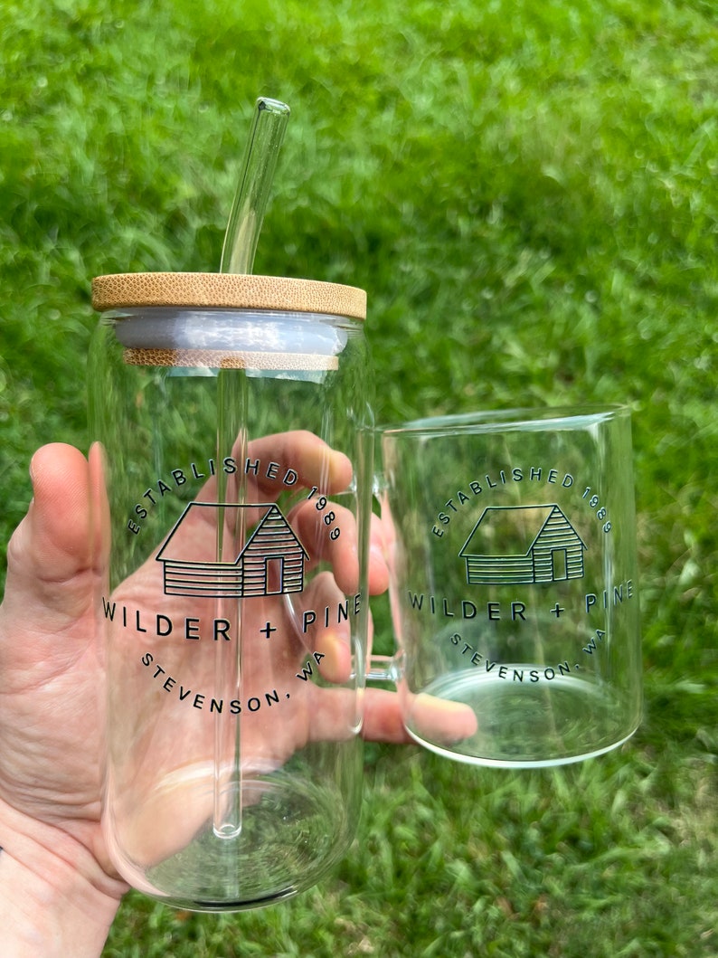 May include: Two clear glass mugs with a bamboo lid and a straw. The mugs have a black and white logo that says "Established 1889 Wilder + Pine Stevenson, WA".