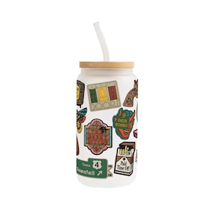 May include: A frosted glass tumbler with a bamboo lid and a clear straw. The tumbler is decorated with colourful stickers, including the words "The Great Divide" and "Paid Time Off".