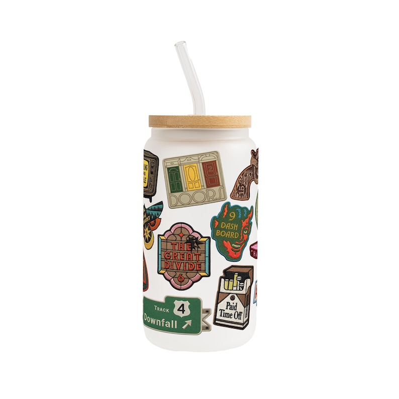 May include: A frosted glass tumbler with a bamboo lid and a clear straw. The tumbler is decorated with colourful stickers, including the words "The Great Divide" and "Paid Time Off".