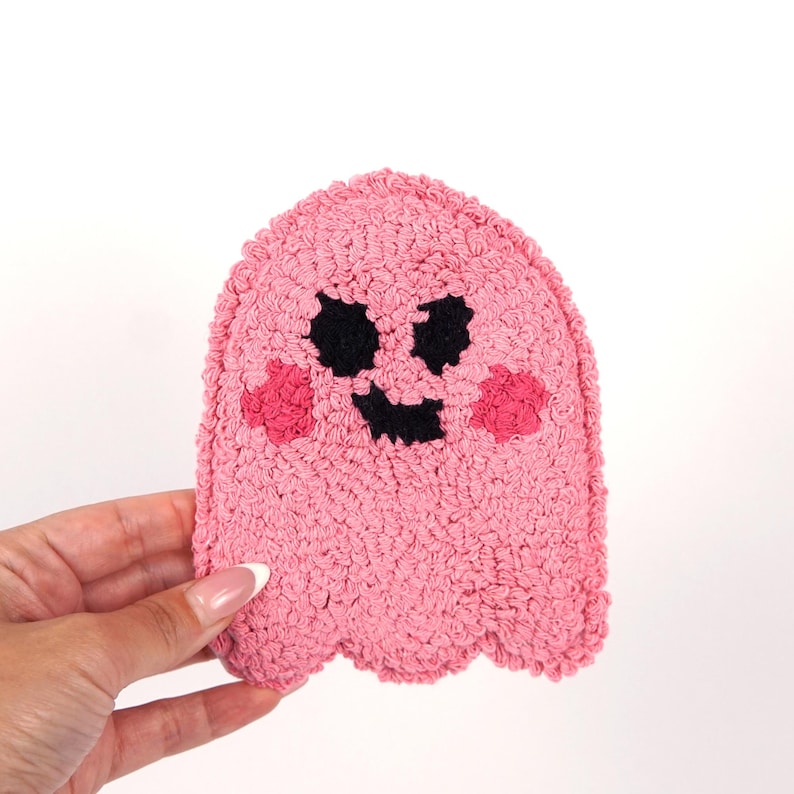 Op de afbeelding: Een roze geest met een zwart lachend gezicht en roze wangen. De geest is gemaakt van een pluche materiaal.