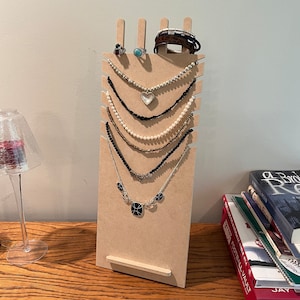May include: A wooden jewelry stand with six necklaces and a bracelet. The necklaces are made of different materials, including pearls, beads, and metal. The bracelet is brown leather with metal accents.