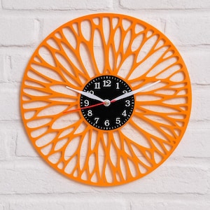 May include: Orange wall clock with a unique, openwork design. The clock face is black with white numerals and hands, and a red second hand. The clock's outer frame has a decorative, floral-like pattern.
