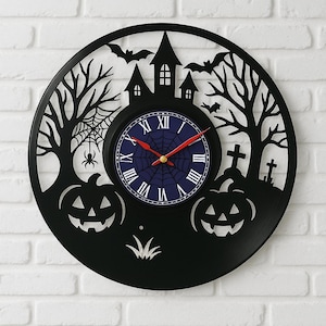 Pode incluir: Relógio de parede preto com tema de Halloween. O relógio apresenta um design assustador com uma casa assombrada, morcegos, árvores, abóboras e uma teia de aranha. O mostrador é azul com algarismos romanos e ponteiros vermelhos.