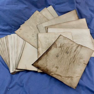 May include: A stack of vintage, off-white paper with a worn, aged appearance. The top sheet has a textured, brown surface.