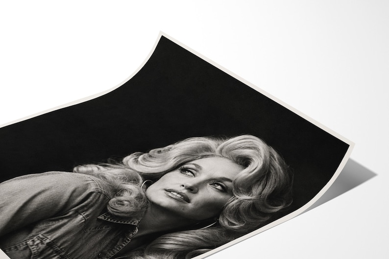 May include: A black and white photographic print featuring a portrait of a person with voluminous, wavy blonde hair styled in a classic bouffant. The subject is wearing a collared shirt and is positioned against a dark, solid black background.