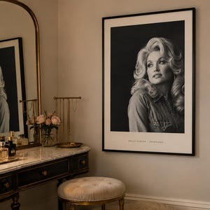 May include: A black and white framed portrait print of Dolly Parton featuring her signature voluminous hair and a denim shirt. The print is displayed in a thin black frame with the text DOLLY PARTON TENNESSEE printed at the bottom center.