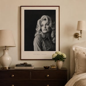 May include: A framed black and white portrait print of Dolly Parton featuring her signature voluminous blonde hair and a denim shirt. The print is displayed in a dark wood frame with a white mat, and the text DOLLY PARTON - TENNESSEE is visible.