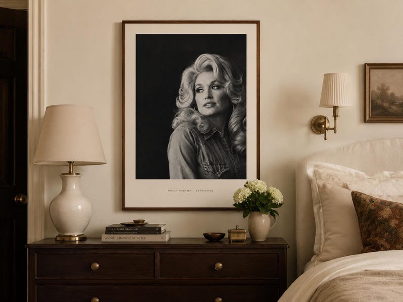 May include: A framed black and white portrait print of Dolly Parton featuring her signature voluminous blonde hair and a denim shirt. The print is displayed in a dark wood frame with a white mat, and the text DOLLY PARTON - TENNESSEE is visible.