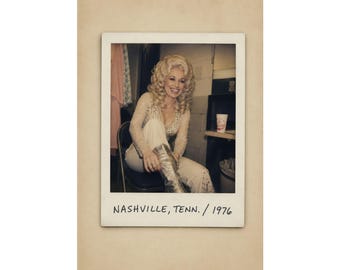 May include: A vintage-style photograph featuring a person with voluminous blonde hair wearing a long-sleeved, embellished top and light-colored pants, sitting on a chair. The photo includes the handwritten text "NASHVILLE, TENN. / 1976" at the bottom.