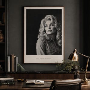 May include: A black and white portrait print of Dolly Parton in a collared shirt, featuring voluminous blonde hair and a side-facing gaze. The print is framed in a thin wooden border with the text Dolly Parton - Tennessee printed at the bottom.