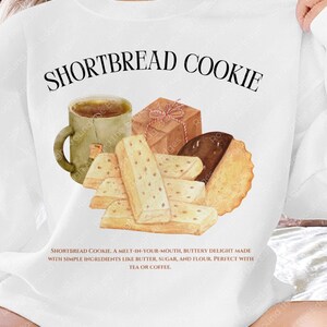 Puede incluir: Camiseta blanca con una ilustración marrón y blanca de galletas de mantequilla, una taza de té y un regalo envuelto. El texto "SHORTBREAD COOKIE" está impreso en negro sobre la ilustración. El texto debajo de la ilustración dice: "SHORTBREAD COOKIE. A MELT-IN-YOUR-MOUTH, BUTTERY DELIGHT MADE WITH SIMPLE INGREDIENTS LIKE BUTTER, SUGAR, AND FLOUR. PERFECT WITH TEA OR COFFEE."