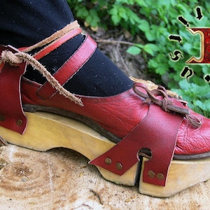 Può includere: Sandali in pelle rossa con suola platform in legno. I sandali hanno un cinturino che avvolge la caviglia e si allaccia nella parte anteriore. La suola platform è alta circa 7,5 cm.