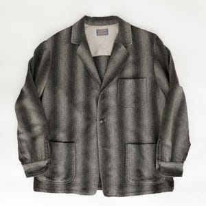 May include: A gray and black striped blazer with a notched collar, three front pockets, and a single-button closure. The jacket has long sleeves with buttoned cuffs and a light-colored lining.