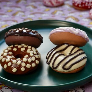 Pode incluir: Quatro donuts decorados em um prato verde. Dois est&atilde;o empilhados, um com cobertura de chocolate e granulado branco, o outro com cobertura de chocolate. Os outros dois donuts t&ecirc;m cobertura branca e chocolate.