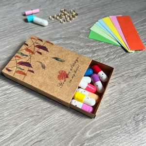 May include: A brown matchbox with a leaf design and the text "You're always in my heart."  The box contains small colorful capsules with smiley faces.