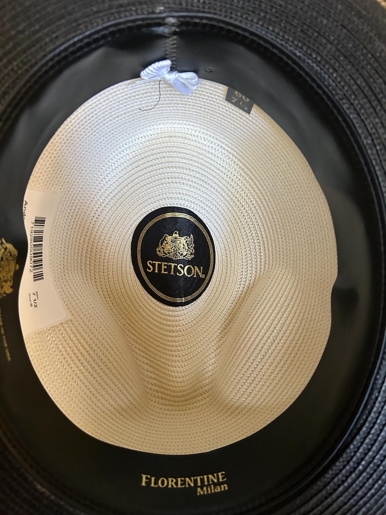 Puede incluir: Vista interior de un sombrero fedora Stetson Florentine Milan negro. El sombrero presenta una corona tejida de color crema y una banda de sudoraci&oacute;n de cuero negro. El logotipo de Stetson es visible en una etiqueta negra y dorada.