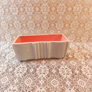 May include: A rectangular planter with a light gray exterior and a coral pink interior. The planter has vertical ribbed detailing on the sides. The container is likely ceramic or porcelain.