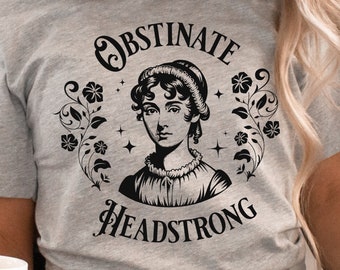 May include: A gray t-shirt with a black and white illustration of a woman with the text "Obstinate Headstrong" in a circle around her.