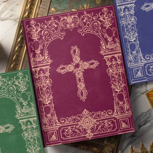 May include: A burgundy journal with a white cross design and ornate floral border. The cover features a decorative archway and intricate details.