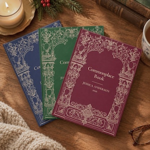 May include: Three hardcover journals in blue, green, and burgundy, each featuring an ornate white architectural frame design. The burgundy journal is personalized with the text Commonplace Book, JESSICA ANDERSON, and the year 2026.