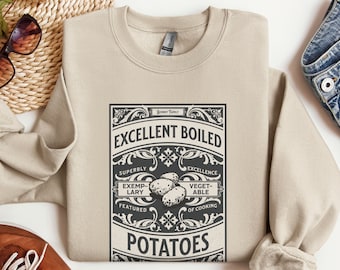 May include: A beige sweatshirt with a vintage-style graphic design featuring the text "Excellent Boiled Potatoes" and a stylized illustration of potatoes. The design includes the text "Bennet Family" and other details.