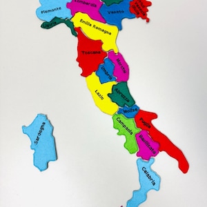 May include: A colorful felt puzzle of Italy, with each region represented by a different color. The names of the regions are printed on each piece. The island of Sardinia is separate.