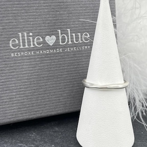 Peut inclure: Une bague en argent sur un présentoir à anneaux blanc. Le présentoir est sur une surface blanche et plumeuse. Le texte "ellie ♥ blue BESPOKE HANDMADE JEWELLERY" est sur un fond gris.