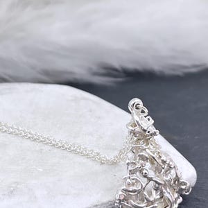 Può includere: Un ciondolo in argento caratterizzato da una struttura complessa, organica e traforata a forma di rete, fissato a una sottile catenina d'argento. Il metallo presenta una finitura lucida e riflettente con numerosi piccoli anelli irregolari.