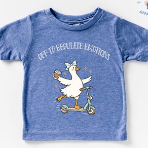 May include: Blue toddler t-shirt with the slogan "OFF TO REGULATE EMOTIONS". The graphic features a white duck with a blue bow, holding a coffee cup, riding a scooter. The shirt has short sleeves and a crew neck.