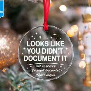 May include: A clear, round Christmas ornament with the text "LOOKS LIKE YOU DIDN'T DOCUMENT IT" in white. The ornament hangs from a red ribbon. The background includes a Christmas tree and a toy soldier.