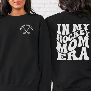 May include: Black sweatshirt with white text that says "In My Hockey Mom Era" on the back and a small hockey stick graphic on the front.