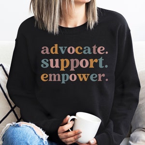 May include: Black sweatshirt with the text "advocate. support. empower." in colorful letters.