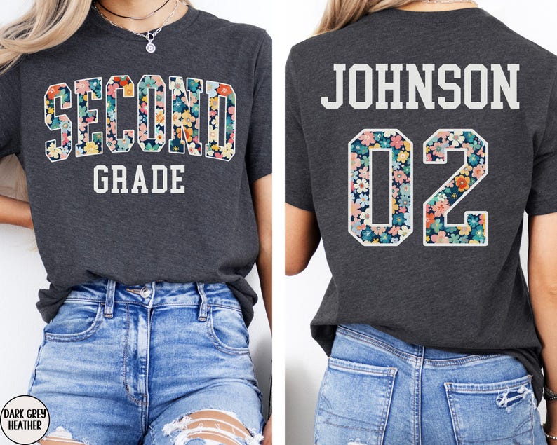 Puede incluir: Camiseta gris oscuro con la inscripci&oacute;n "SECOND GRADE" en un dise&ntilde;o floral en la parte delantera. La parte trasera de la camiseta muestra "JOHNSON 02" con detalles florales. La camiseta se combina con vaqueros azules.