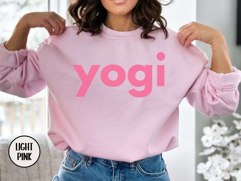 Może przedstawiać: R&oacute;żowa bluza z nadrukiem słowa "yogi" w dużym, pogrubionym, r&oacute;żowym foncie.