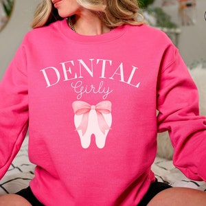 May include: Pink sweatshirt with the text "Dental Girly" and a pink bow on a white tooth graphic.