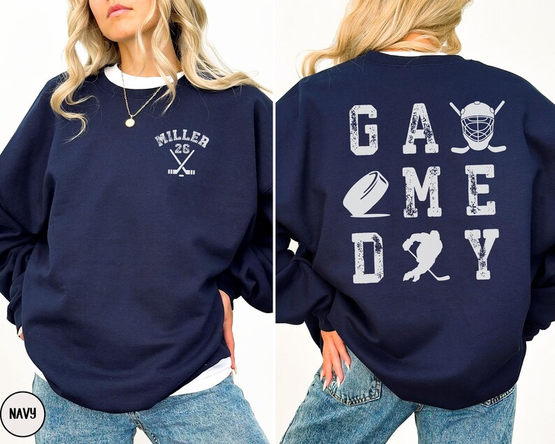 May include: Navy blue sweatshirt with a white graphic on the back that says "GAME DAY" with hockey-themed imagery. The front of the sweatshirt has a white graphic with the text "MILLER 26" and crossed hockey sticks.