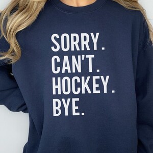 May include: Navy blue sweatshirt with white text that reads "SORRY. CAN'T. HOCKEY. BYE."