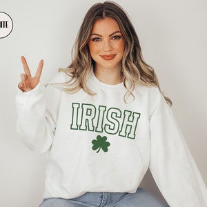 Op de afbeelding: Wit sweatshirt met het woord "IRISH" in groene en zwarte letters en een groene klaver.