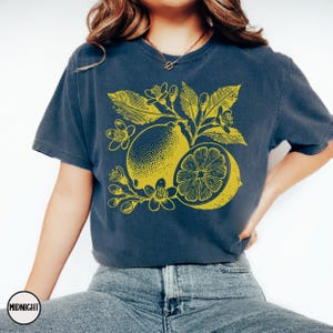 Op de afbeelding: Een marineblauw t-shirt met een gele citroenprint. De citroen is omringd door gele bladeren en bloemen.