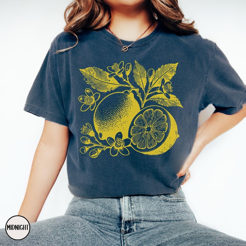 Op de afbeelding: Een marineblauw t-shirt met een gele citroenprint. De citroen is omringd door gele bladeren en bloemen.