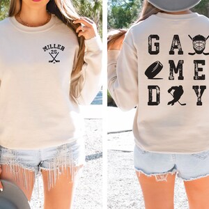 May include: A beige sweatshirt with the text "MILLER 26" on the front and "GAME DAY" with hockey-related graphics on the back.