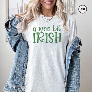 以下が含まれることがあります： 緑色の「a wee bit IRISH」の文字が入った、明るい灰色の長袖シャツ。柔らかい素材で作られており、聖パトリックの日のようなカジュアルな場面に最適です。快適な着心地です。